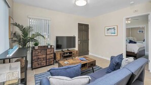 A modern living room with a sofa, coffee table, TV, and a plant. - Quiet, Comfortable Sunset Cliffs Ocean Beach Apartment – Walk to Beach! (San Diego)