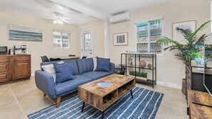 A living room with a blue sofa, a wooden coffee table, and a bookshelf. - Quiet, Comfortable Sunset Cliffs Ocean Beach Apartment – Walk to Beach! (San Diego)