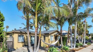 A two-story house with a yellow exterior, surrounded by palm trees and a hammock. - Quiet, Comfortable Sunset Cliffs Ocean Beach Apartment – Walk to Beach! (San Diego)