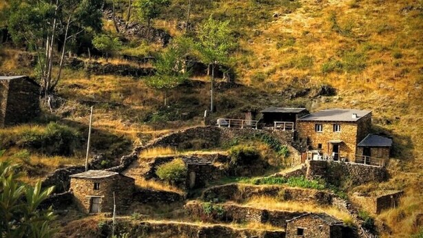 Een landelijk landschap met terrassen van steen en een stenen huis met een balkon.