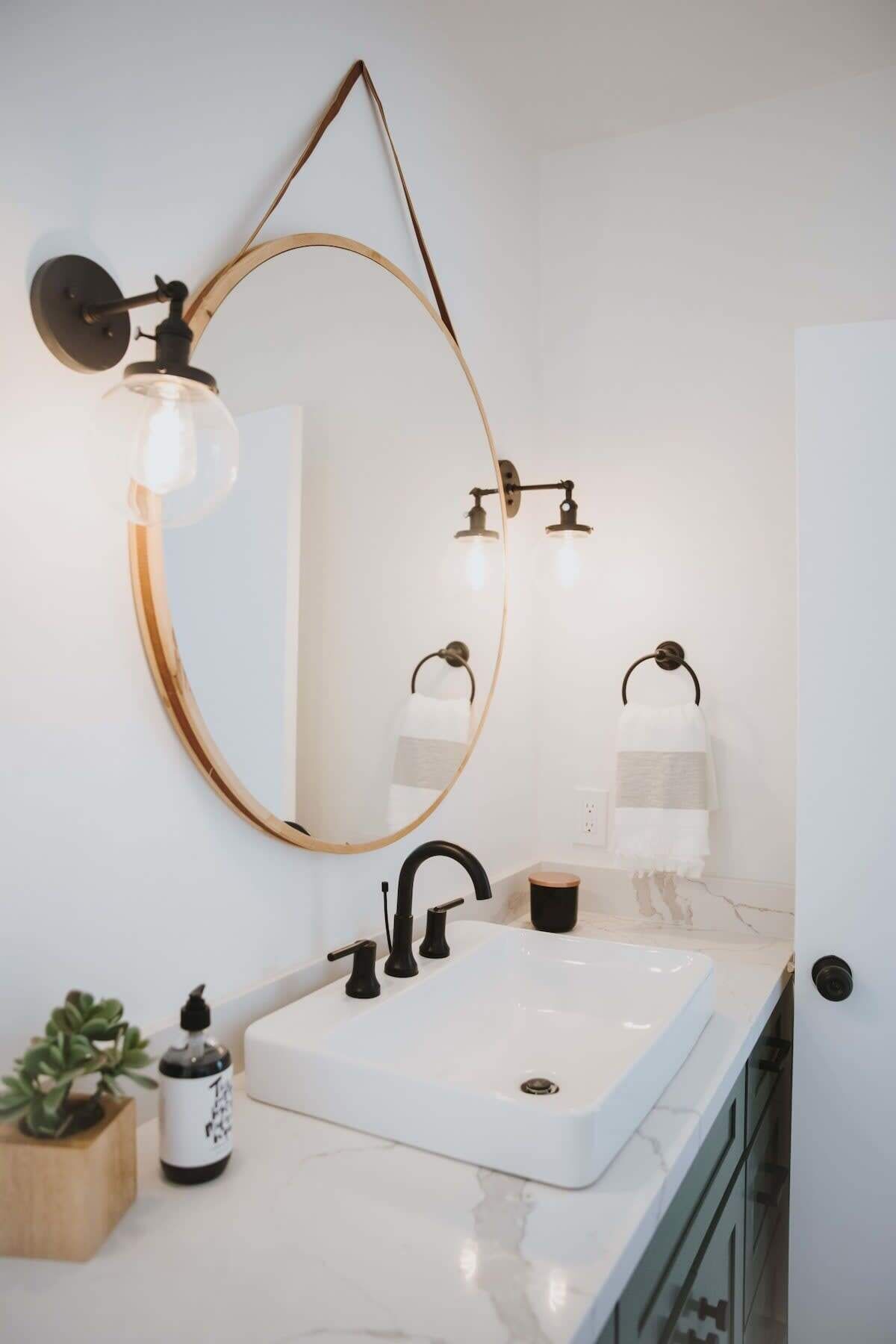 A bathroom with a white sink, a round mirror with a gold frame, and two wall-mounted lights.