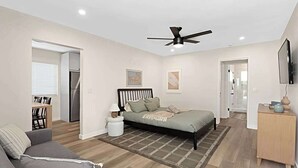 Ein modernes Schlafzimmer mit Bett, Deckenventilator, Fernseher und einer kleinen Schreibtischzeile.