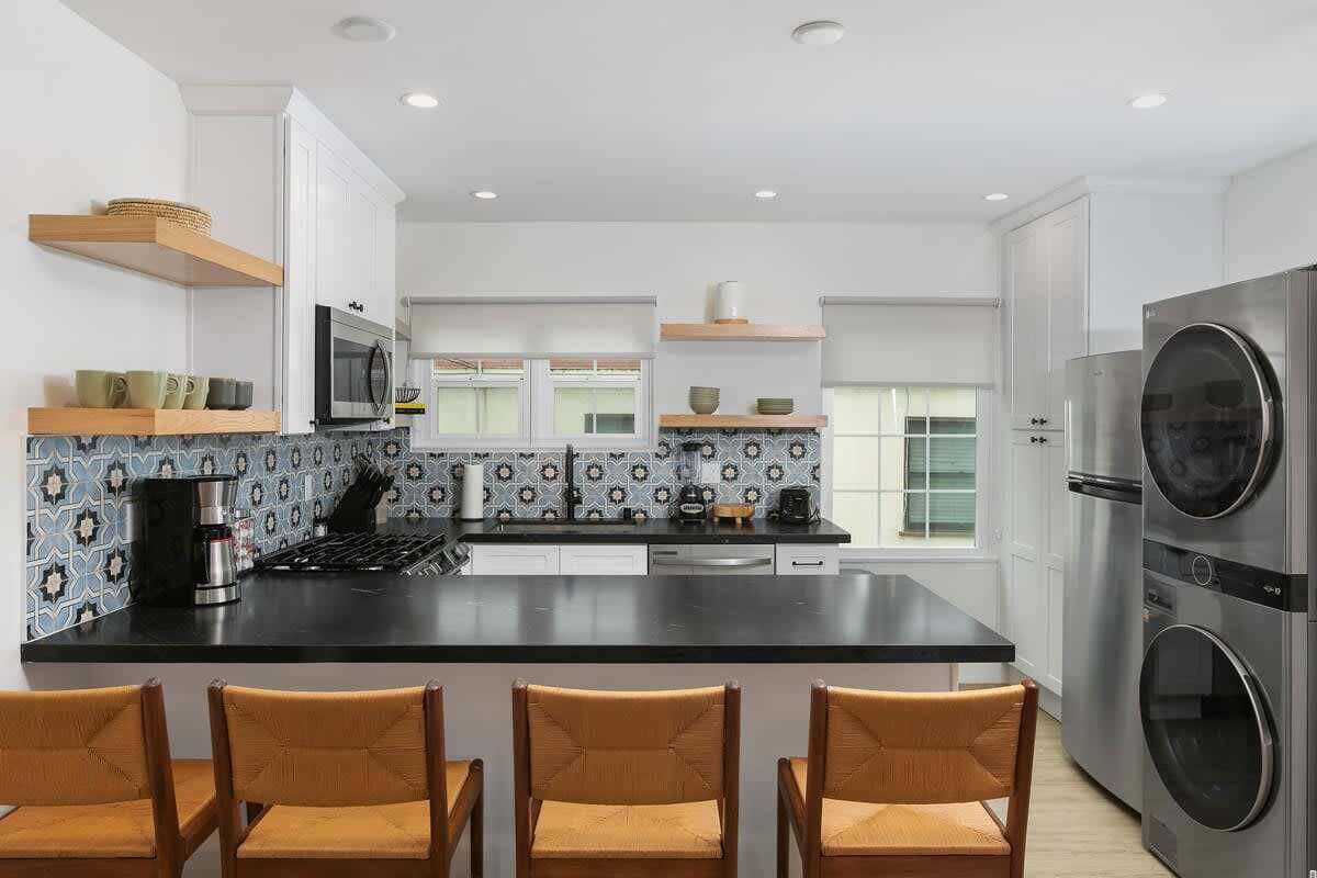 A modern kitchen with a central island, bar stools, a built-in oven, and a stainless steel refrigerator.