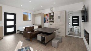 A modern, well-lit living room with a sofa, a coffee table, and a TV. There is a door with a window, a cabinet, and a painting on the wall. - Chic Studio in Banker's Hill, Steps to Balboa Park (San Diego)