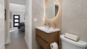 A modern bathroom with a wooden vanity, a round mirror, and a toilet. - Chic Studio in Banker's Hill, Steps to Balboa Park (San Diego)