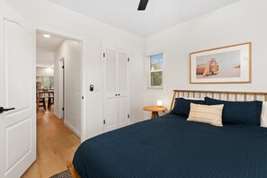Un dormitorio con una cama grande, puertas blancas, una mesita de noche con lámpara y un cuadro en la pared.