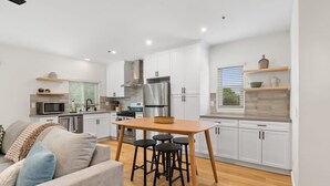 A modern kitchen with white cabinets, a stainless steel refrigerator, and a wooden dining table with stools.