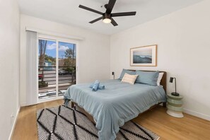 A bedroom with a bed, a ceiling fan, a window with a view, and a framed picture on the wall.