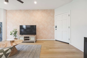 Ein modernes Wohnzimmer mit einem Flachbildfernseher, einem Holztisch, einer Wand mit Muster und einer Tür.