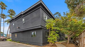 A modern two-story building with a dark exterior, a parking lot, and a small tree in the foreground. - Stylish 2BD Peek-a-boo Ocean View High-End Stay (Solana Beach)