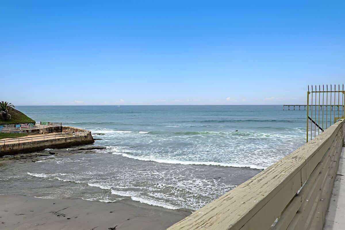 Blick auf die Küste mit einem Sandstrand, einem Pier in der Ferne und einer Betonmauer.