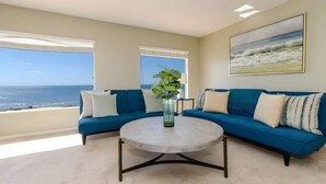 A living room with a blue sofa, a round coffee table, and a large window offering a view of the ocean. - 4BR Home Sunset Cliffs Oceanfront - Cliffside View (San Diego)