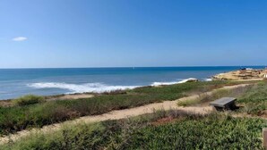 A coastal landscape with a sandy beach, sparse vegetation, and a clear blue sky. - 4BR Home Sunset Cliffs Oceanfront - Cliffside View (San Diego)