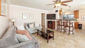 A living room with a sofa, coffee table, and a TV. There is a kitchen area with a dining table and chairs.