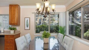 A dining area with a glass table, white upholstered chairs, a wooden cabinet, and a chandelier.