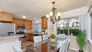 A modern kitchen with wooden cabinets, stainless steel appliances, and a dining area with a glass table and chairs.