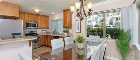 A modern kitchen with wooden cabinets, stainless steel appliances, and a dining area with a glass table and chairs.