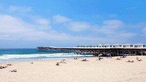 A beach with a pier extending into the ocean, featuring a building with multiple levels and a beach umbrella.