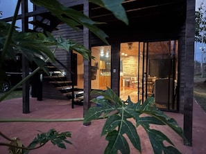 A modern building with a wooden exterior and a glass door leading to an interior with a dining area and a staircase. - Charming Private Retreat in the Rainforest near Jaco (San Gabriel)