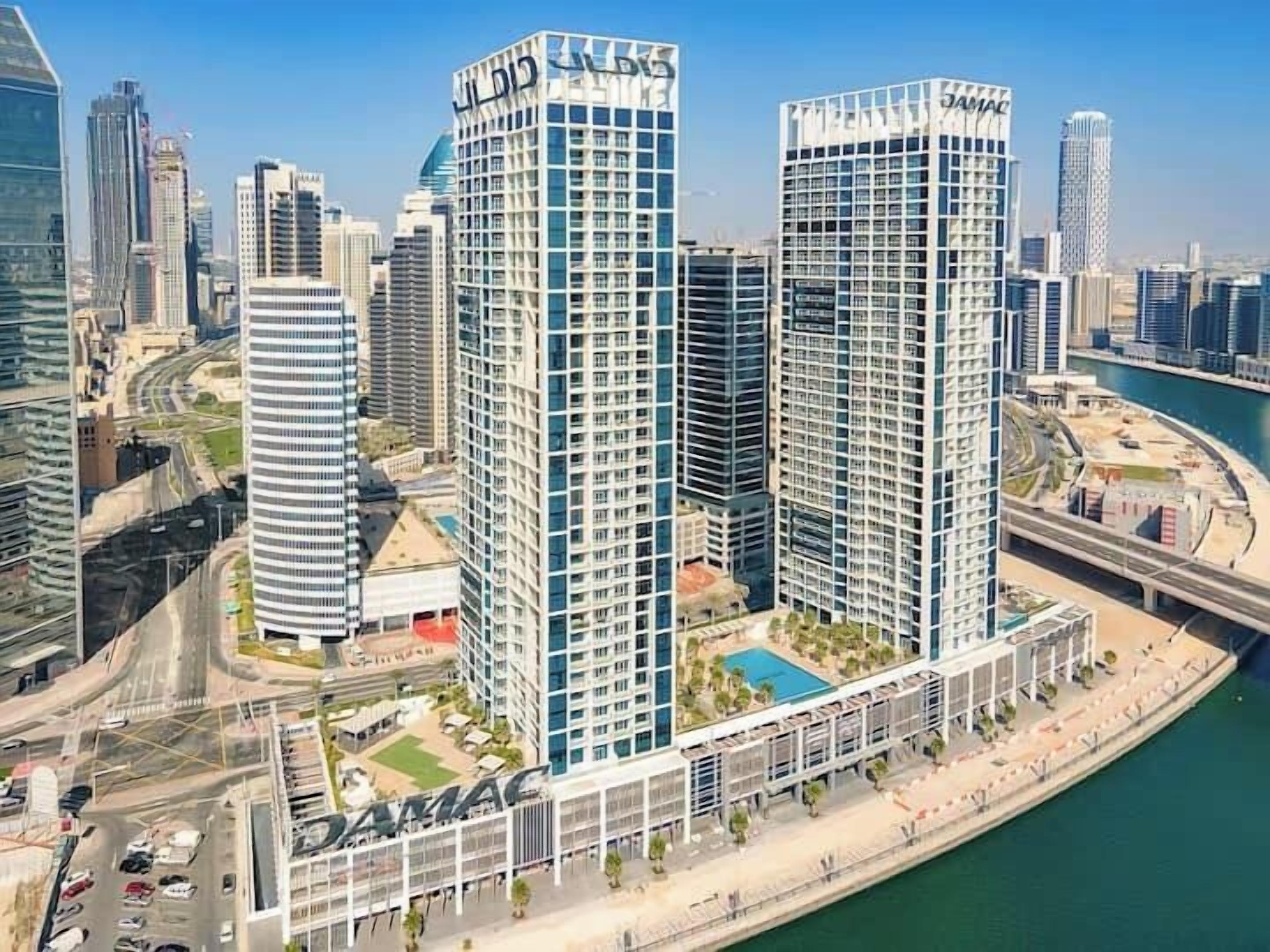 Un edificio de gran altura con fachada de vidrio moderna, situado cerca de una masa de agua y rodeado de otros edificios altos.