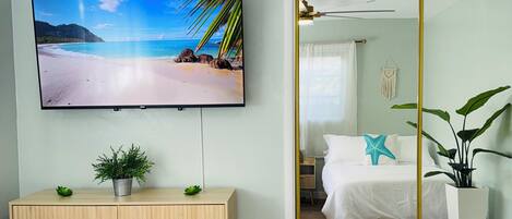 Une chambre à coucher avec un lit, un téléviseur fixé au mur, une commode en bois et un miroir.