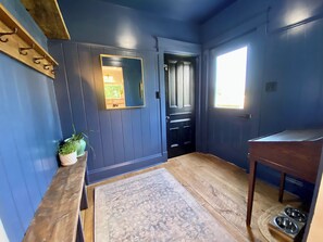Una habitación con un banco de madera, un tapete, un espejo, una puerta y una ventana.
