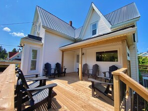 Una casa con terraza de madera, mobiliario exterior y un porche cubierto.