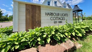 Placa para as Cottages Harbour Lights, com um céu claro e vegetação em primeiro plano.