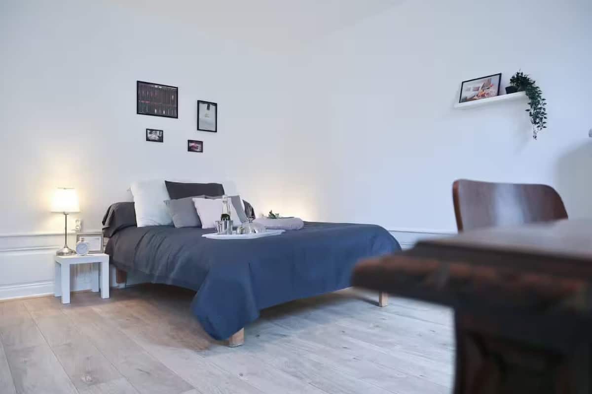 A bedroom with a bed, bedside table, lamp, and a chair.
