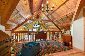 A cozy attic bedroom with a sloped ceiling, a wooden desk, a chair, a patterned rug, and a view of the outdoors.