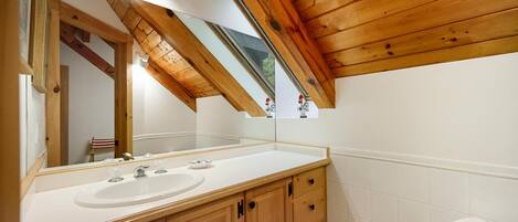 Een badkamer met houten balken, een grote spiegel, twee wastafels en een toilet.