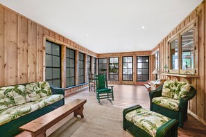A spacious room with wooden walls and large windows, furnished with a sofa, chairs, and a bench.