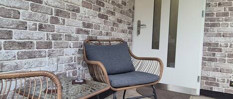 A brick-walled room with two wicker chairs and a glass table.