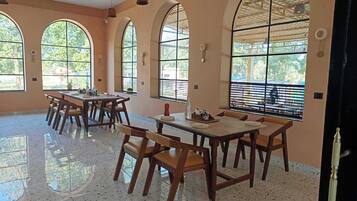 A spacious dining area with high arched windows, wooden tables, and chairs.