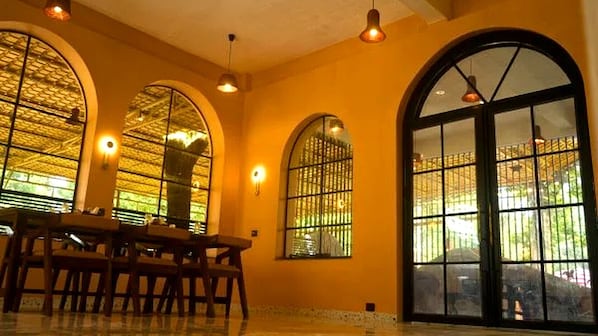 A dining area with a table and chairs, large arched windows with metal bars, and pendant lighting.
