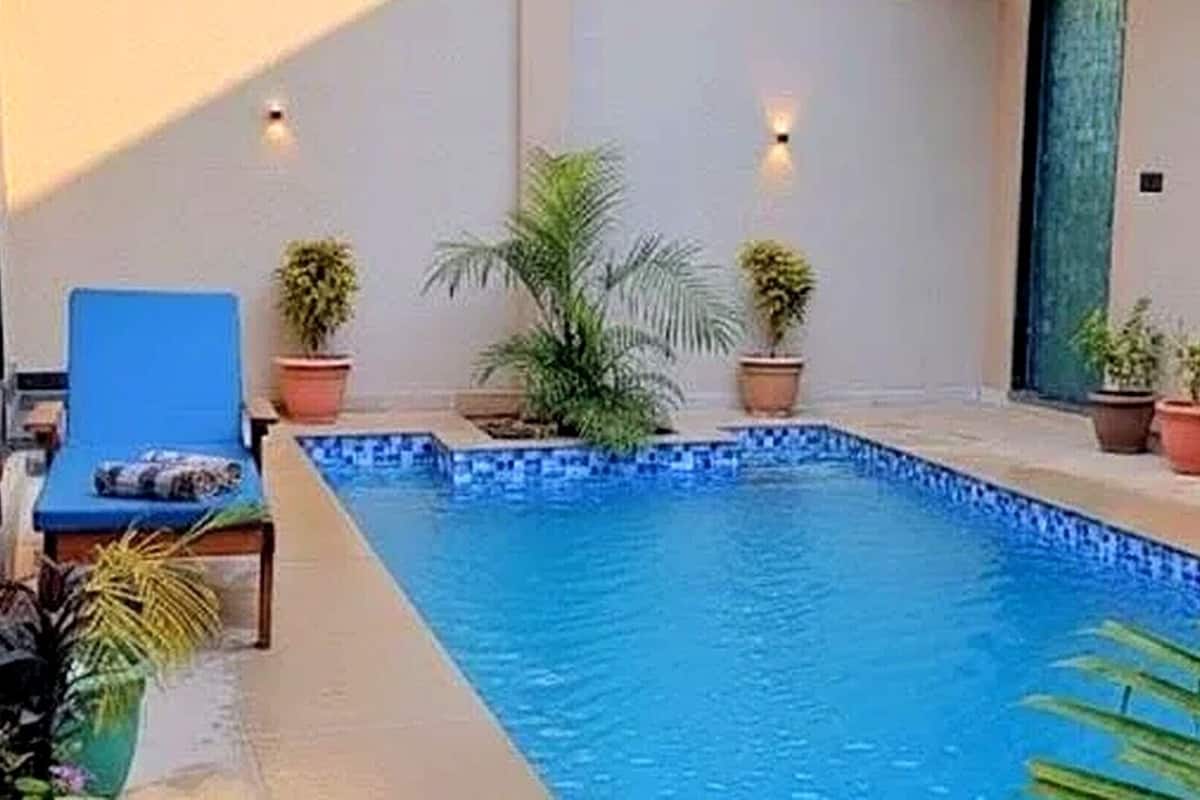 Une piscine dont le bord est recouvert de carreaux bleus, entourée de plantes en pot et agrémentée d’un fauteuil de jardin bleu.