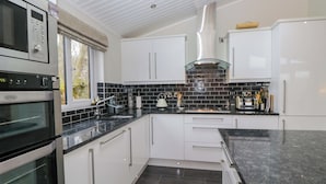 A modern kitchen with white cabinets, a black countertop, and a Belling oven. - Waters Edge Lodge (Windermere)