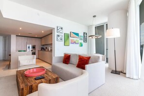 A modern living room with a grey sofa, a wooden coffee table, and a red bowl. There is a kitchen in the background with a microwave and a sink. - Lyfe Resort 1 Br /1 Bath Steps from Beach & Beautiful OceanViews up to 4 guests (Hollywood)