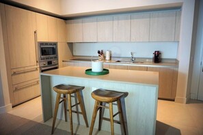 A modern kitchen with wooden cabinets, a built-in oven, a sink, and two bar stools. - Lyfe Resort 1 Br /1 Bath Steps from Beach & Beautiful OceanViews up to 4 guests (Hollywood)