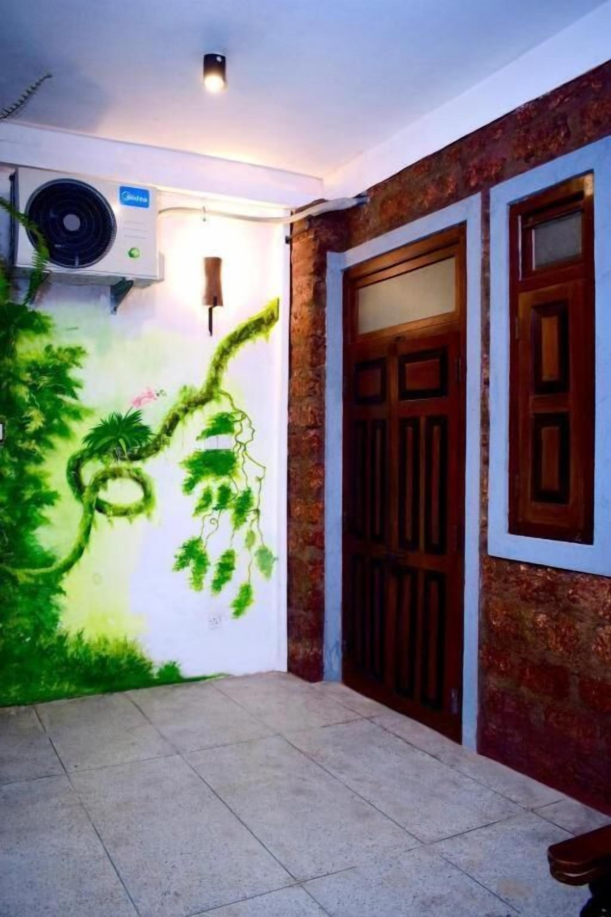 A room with a mural of a tree and hanging vines, a ceiling fan, and a wooden door with glass panels.