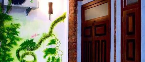 A room with a mural of a tree and hanging vines, a ceiling fan, and a wooden door with glass panels.