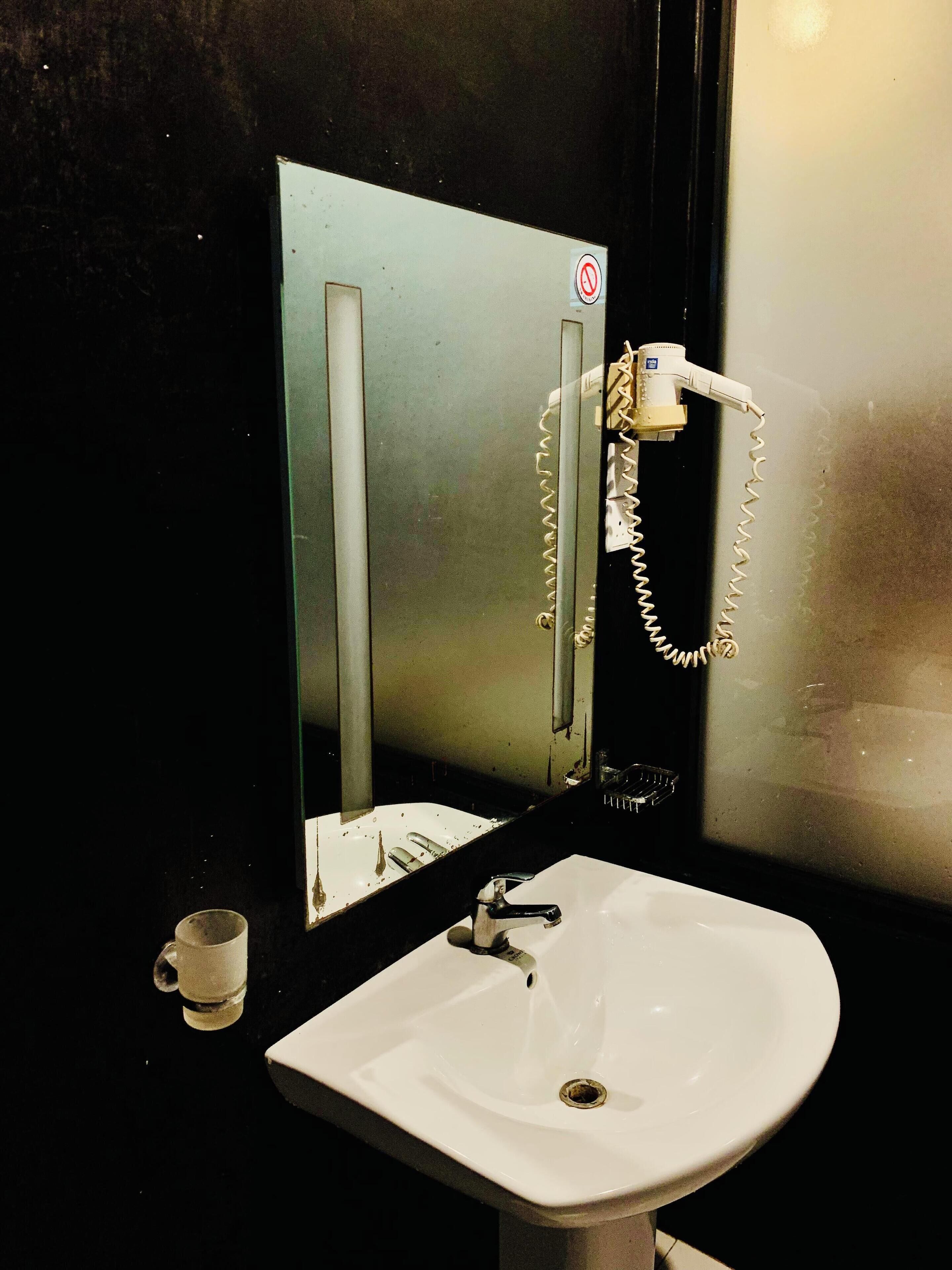 A bathroom with a sink, a mirror, and a hairdryer mounted on the wall.