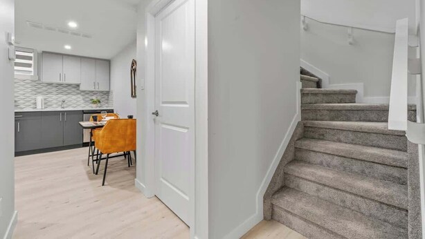 Una cocina moderna con armarios grises, un comedor con mesa y sillas, y una escalera con alfombra.