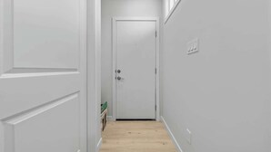 Un pasillo estrecho con paredes blancas y suelo de madera que conduce a una puerta cerrada.