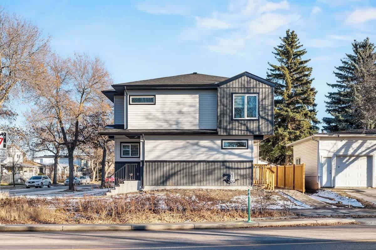 A two-story residential building with a garage, a front yard with a wooden fence, and a street view with parked cars and leafless trees.