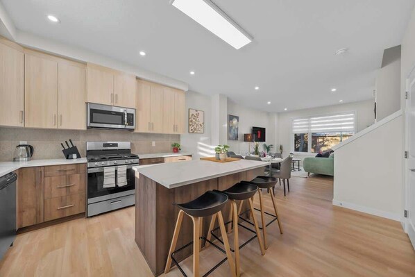 A modern kitchen with wooden cabinets, a central island with stools, a microwave, and an oven.
