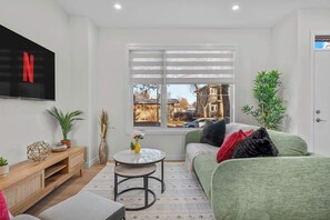 A modern living room with a green sofa, a small round table, and a TV mounted on the wall.