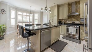 A modern kitchen with a central island, stainless steel appliances, and a large window providing natural light. - Spacious 7BR Home with Private Yard & Fast WiFi! (Brampton)