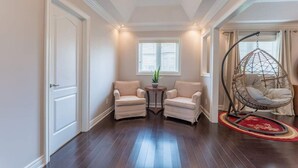 A room with dark hardwood flooring, two armchairs, a small round table with a plant, and a hanging chair with a cushion. - Spacious 7BR Home with Private Yard & Fast WiFi! (Brampton)