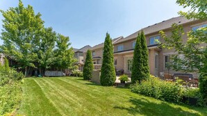 A residential area with a well-maintained lawn, tall trees, and a brick building with multiple windows. - Spacious 7BR Home with Private Yard & Fast WiFi! (Brampton)